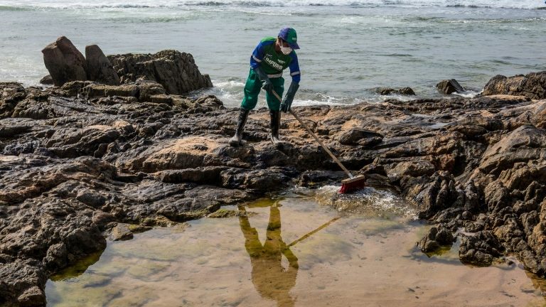 Funcionário da prefeitura limpa petróleop na praia da Pedra do Sal, em Salvador, e, 23 de outubro  - AFP