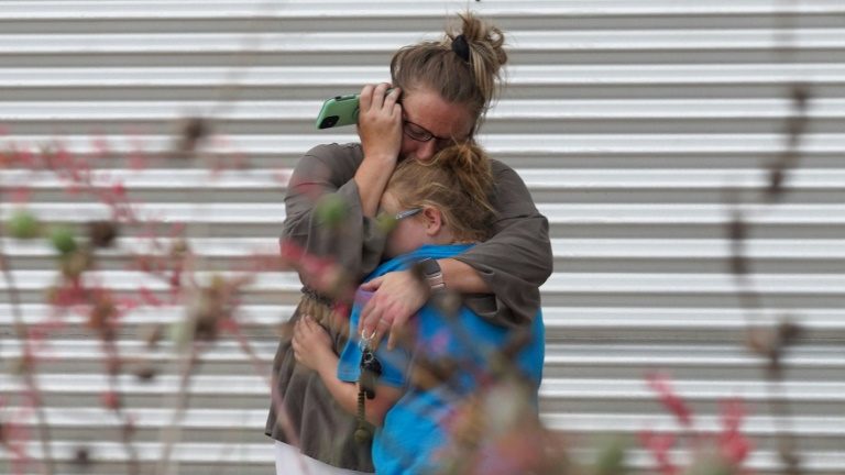 Mulher chora e abraça uma menina enquanto fala pelo telefone na área externa do Centro Cívico Willie de Leon, em Uvalde, Texas, em 24 de maio de 2022 - AFP