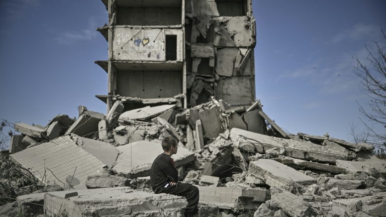 Criança sentada perto de prédio destruído por bombardeio em Kramatorsk - AFP